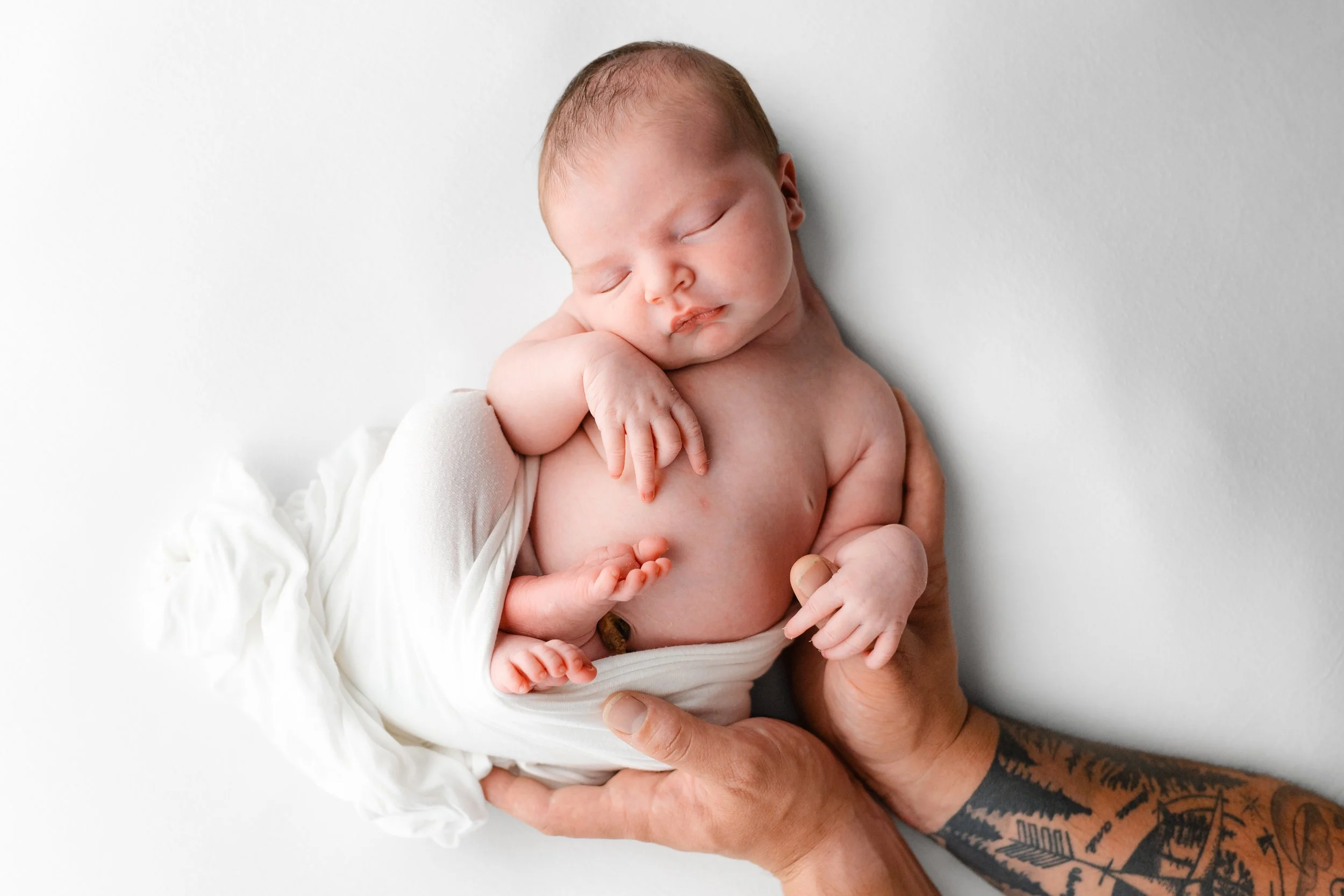 A newborn baby on white fabric with dad's hands around her body