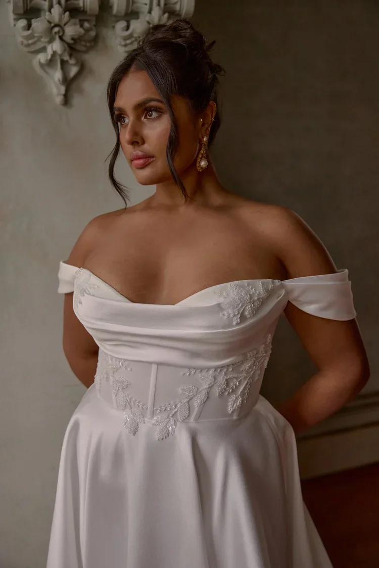 Brisbane bride wearing Alaska gown by Anna Campbell, off-the-shoulder wedding dress with floral embroidery and a sheer corset bodice, standing outdoors in front of a decorative stone staircase and wooden windows.