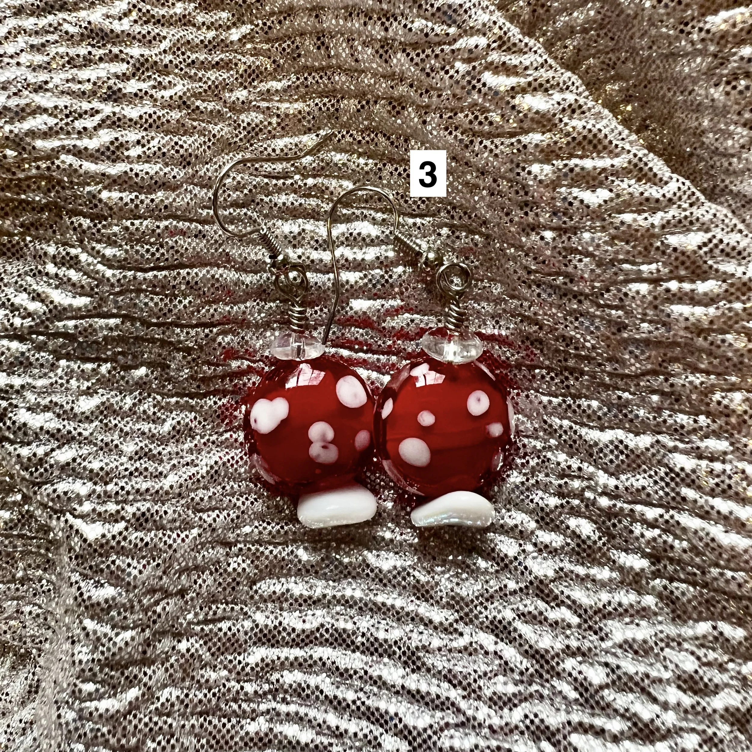red and white glass lampwork beaded earrings that look a little like toadstools laying on a silver backdrop