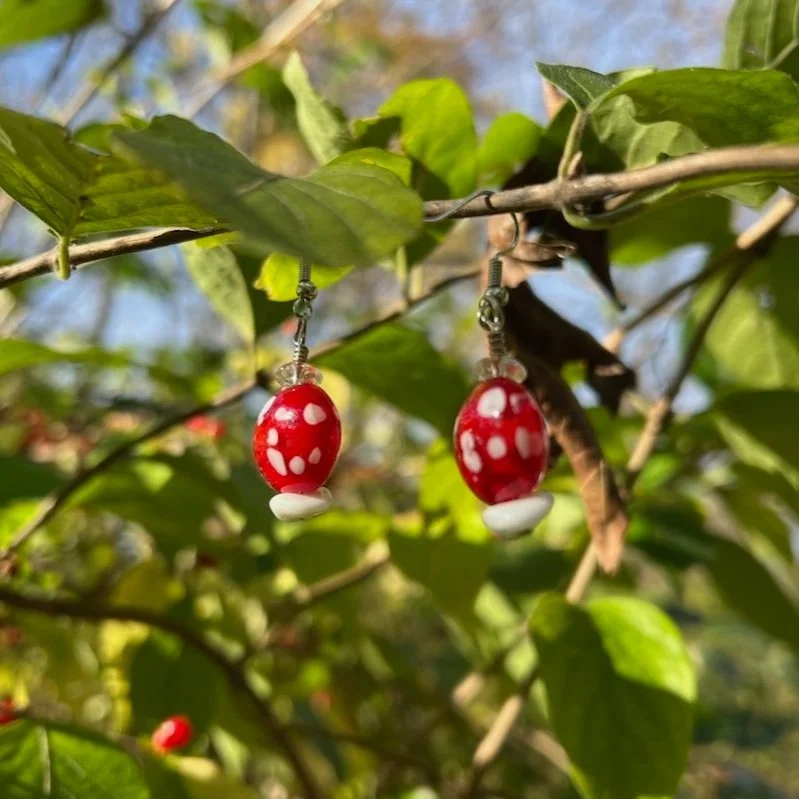 red and white glass lampwork beaded earrings that look a little like toadstools, a second view in the sunlight