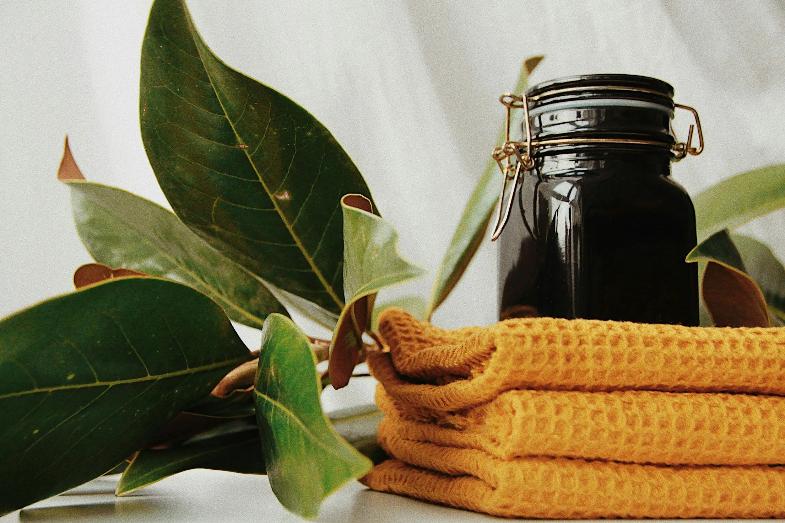 A stack of two yellow towels, a black jar, and green leaves