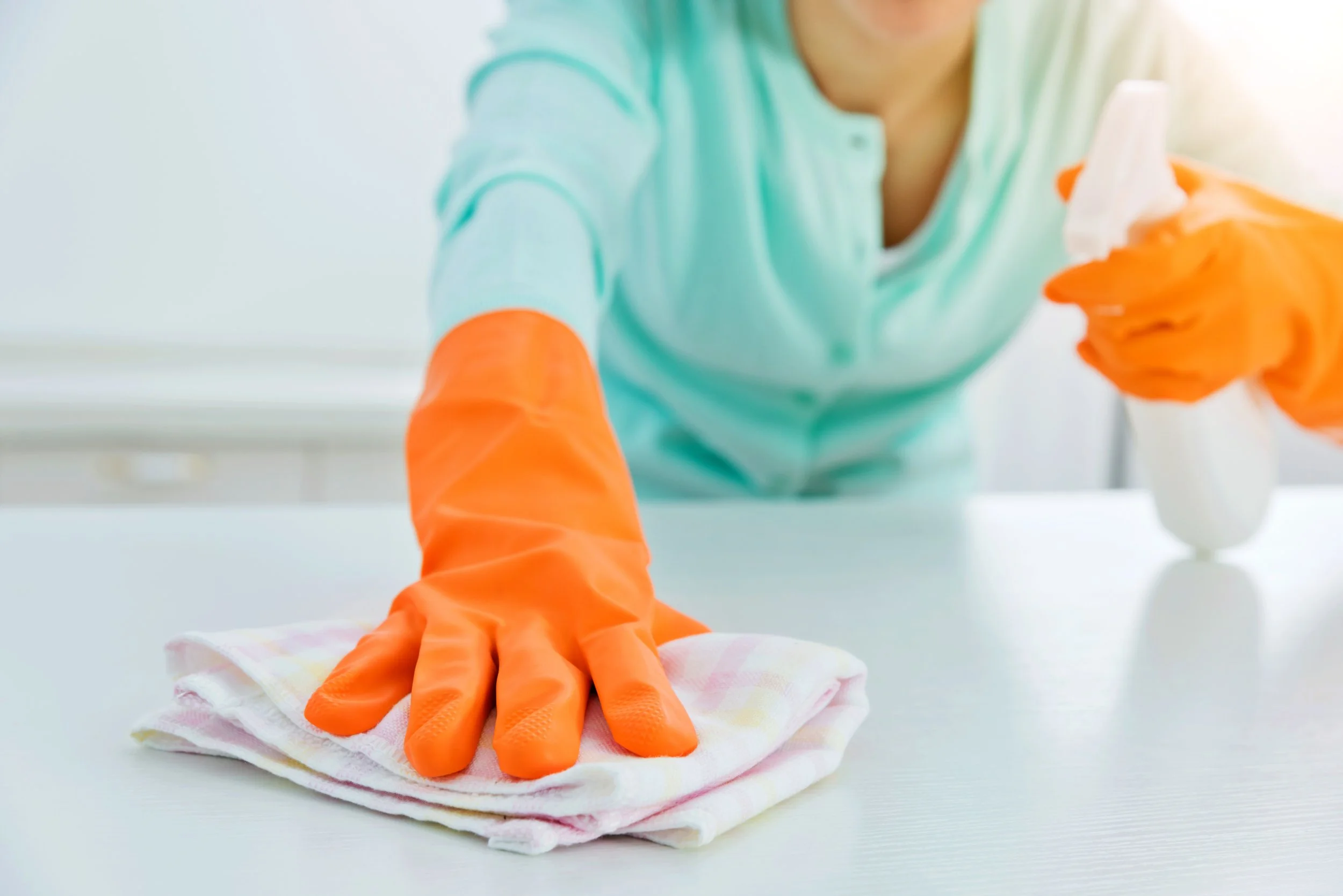 Person wearing orange gloves cleaning a white surface with a cloth.