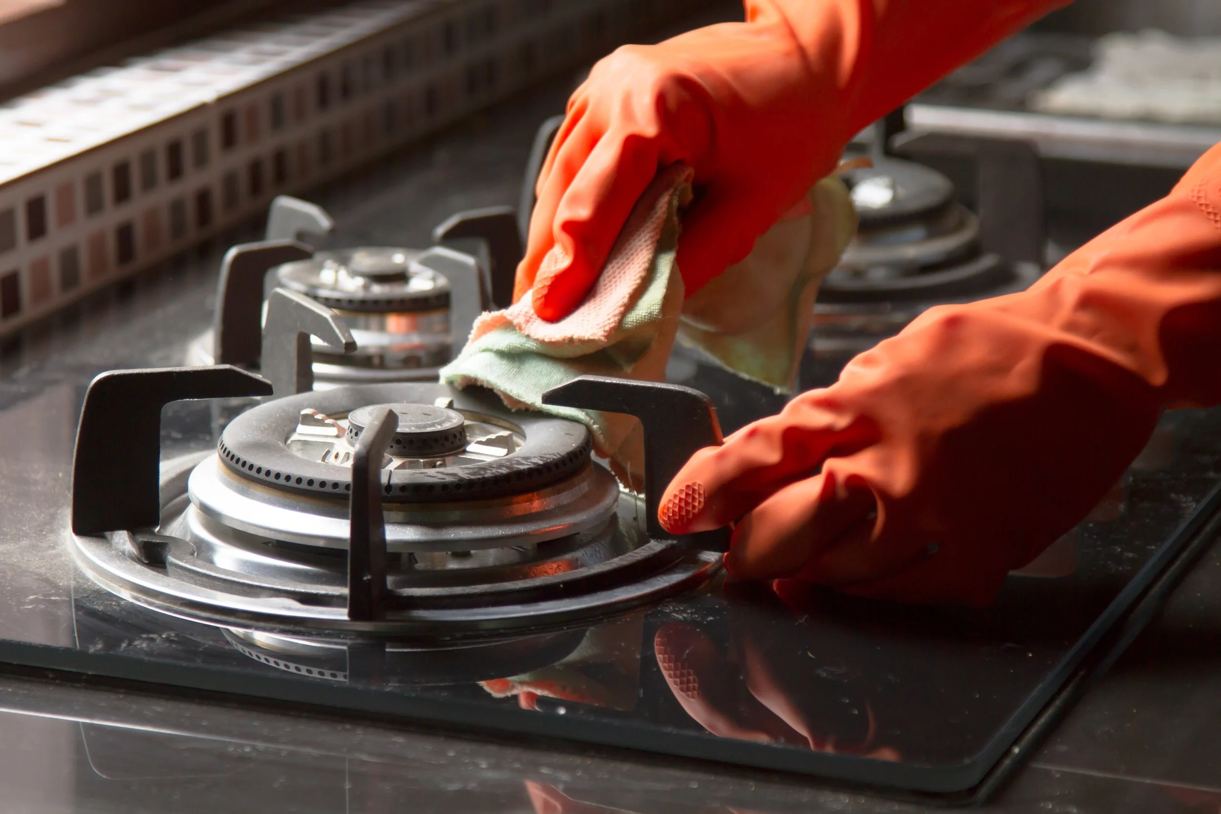 Person wearing orange gloves cleaning a stove burner with a cloth.