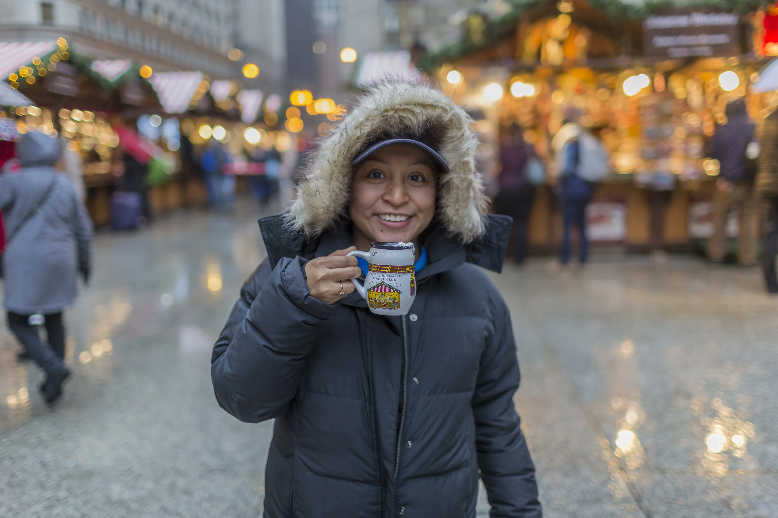 Person wearing a winter coat holding a mug at a festive market.