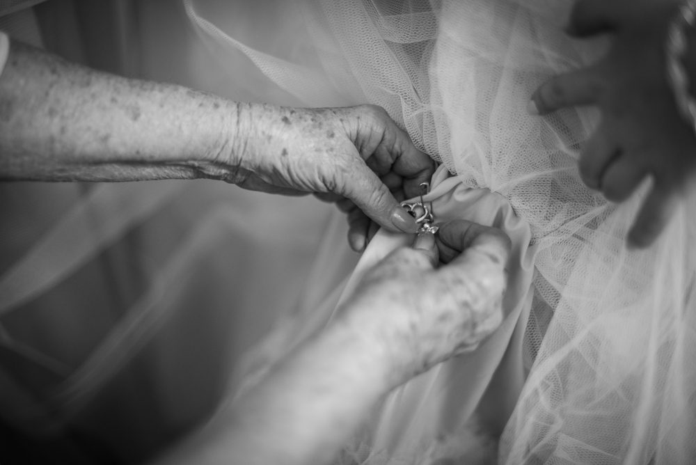 grandmother's hands shown pinning charms onto bride's dress