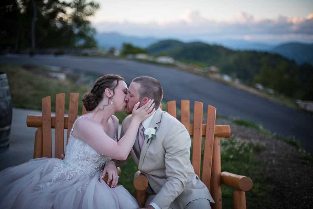 bride and groom kissing outside while sitting in chairs and overlooking mountains