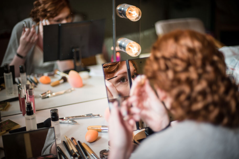 bride getting ready for her wedding, putting on makeup while looking in mirror