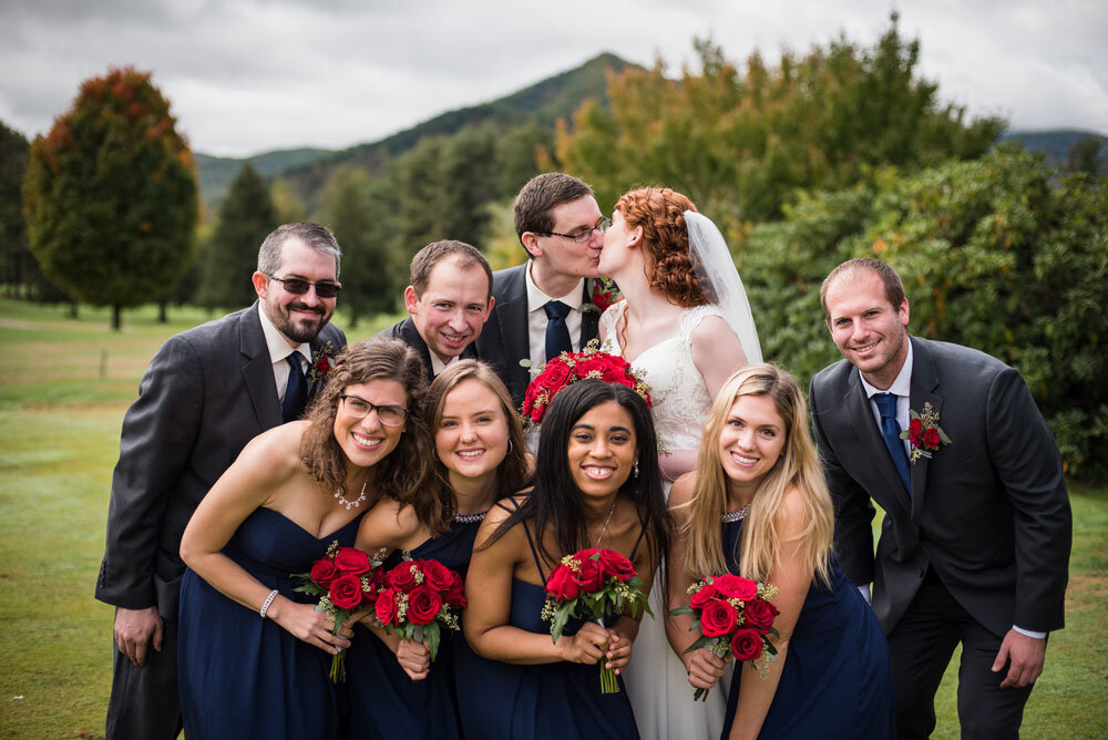 Bride and groom kissing while surrounded by their bridal party.