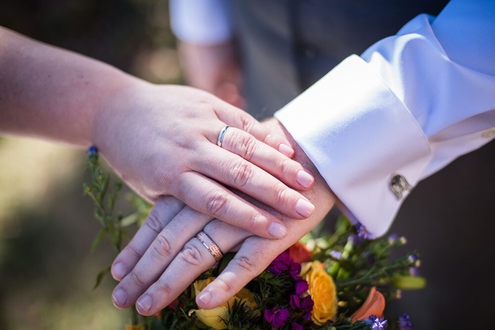 Bride and groom's hands displaying their wedding rings atop a flower bouquet