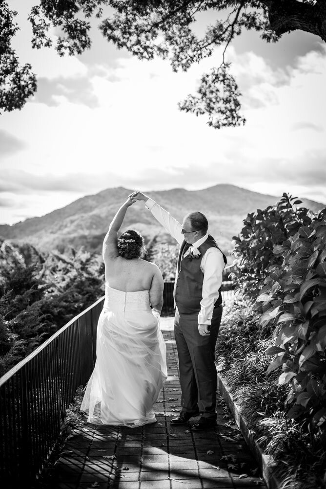 Groom twirling his bride with Lake Junaluska and mountains in the background