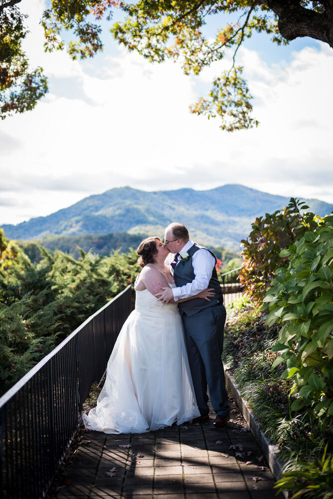 Bride and groom embracing and kissing with the mountains around Lake Junaluska in the background.