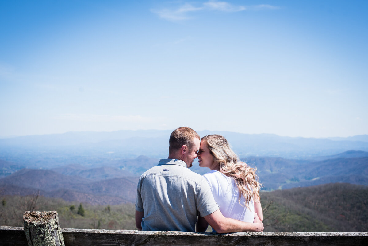 Bride and groom sit on bench overlooking mountains while looking at each other