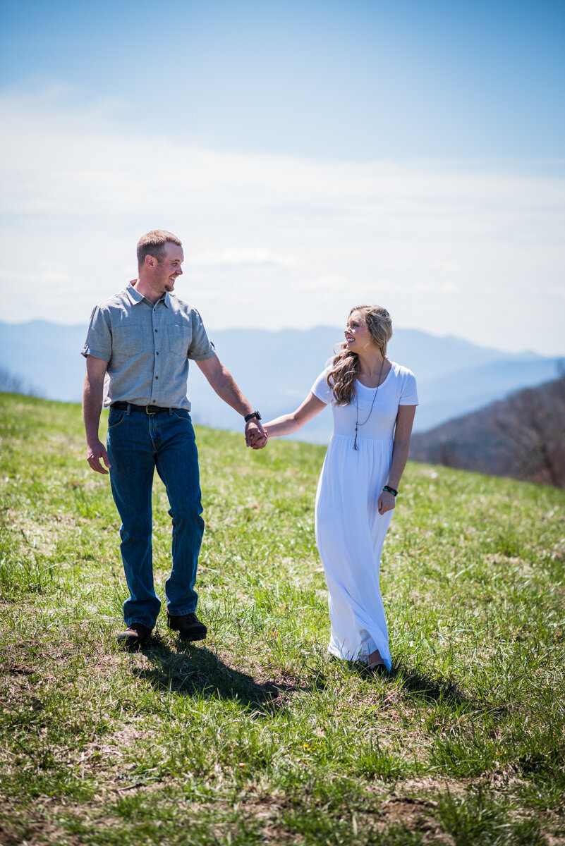 Bride and groom holding hands and looking at each other while walking through grass after mountaintop elopement