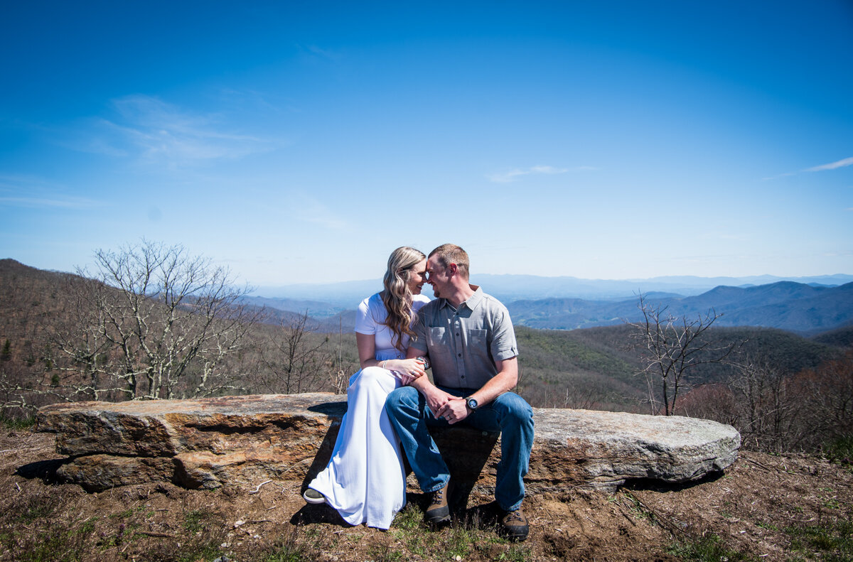 Bride and groom looking at each other while sitting on a rock overlooking mountains