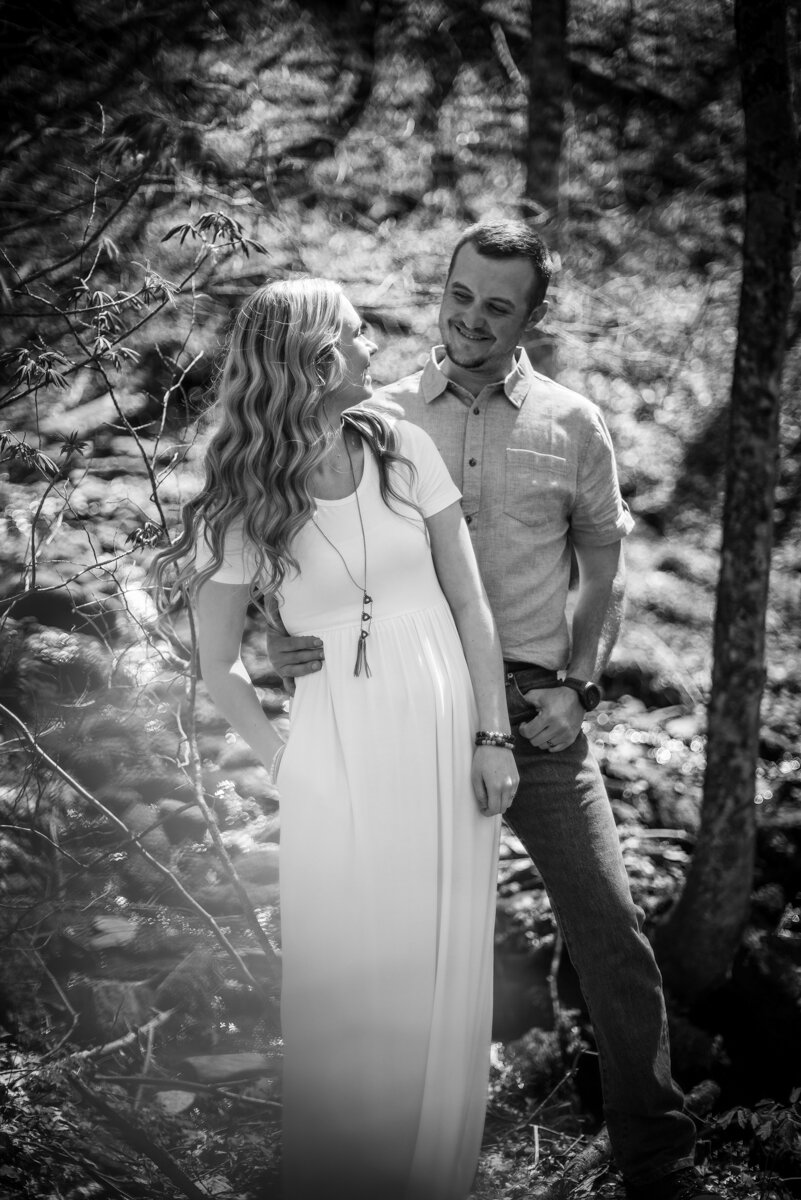 Bride and groom smiling at each other while standing in a wooded area