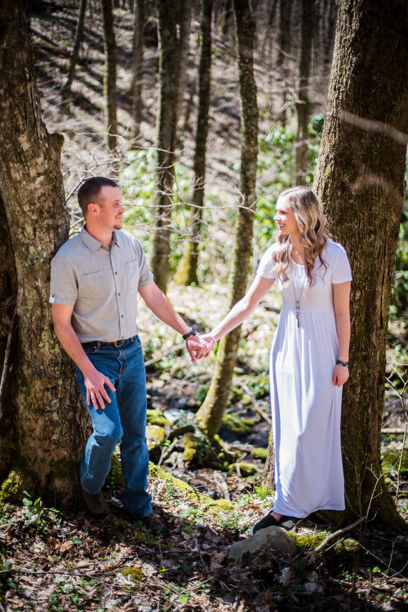 Bride and groom holding hands and looking at each other in wooded area after mountaintop elopement