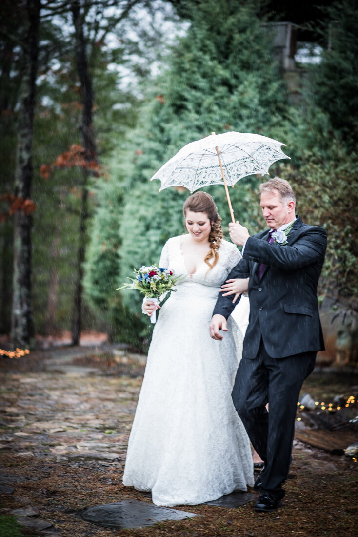Bride and father of the bride walking down the aisle in rain under white umbrella