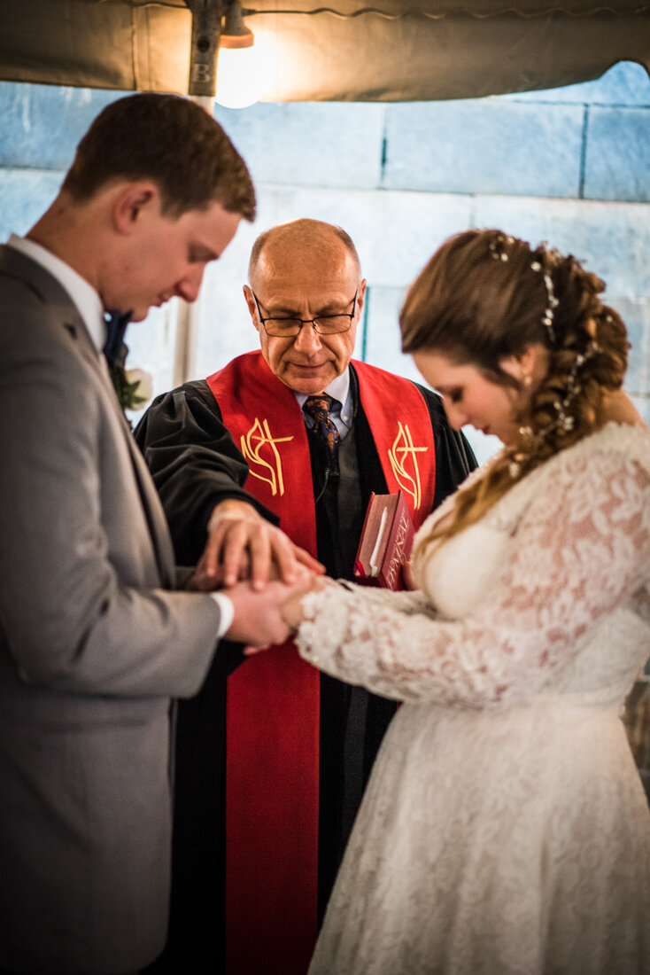 Minister praying with bride and groom during wedding ceremony