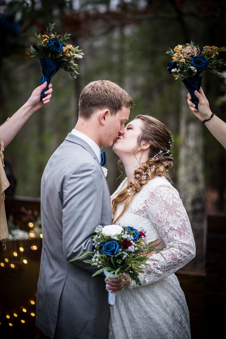 Bride and groom kissing on wedding day under floral arrangements