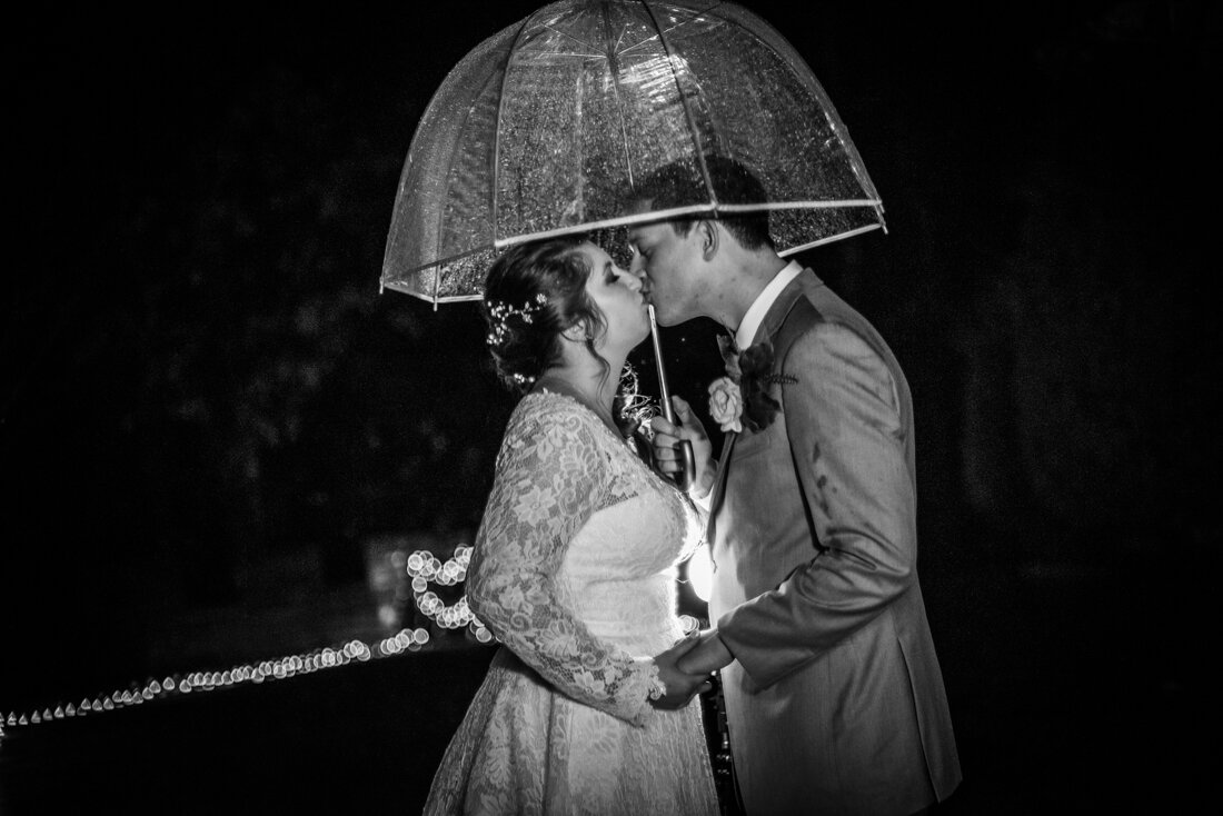 Bride and groom kissing in the rain under a clear dome umbrella