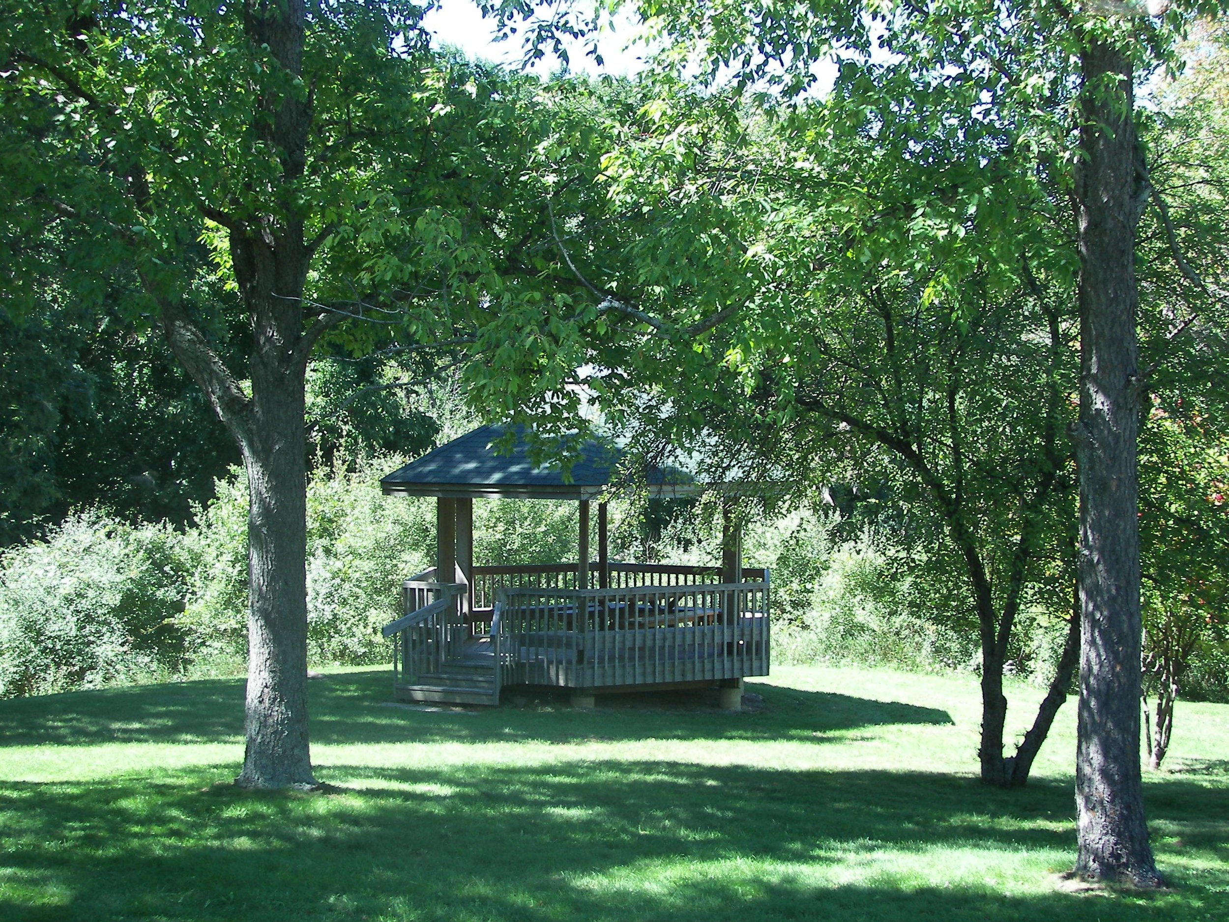 small, open air structure with benches and roof, surrounded by trees and greenery