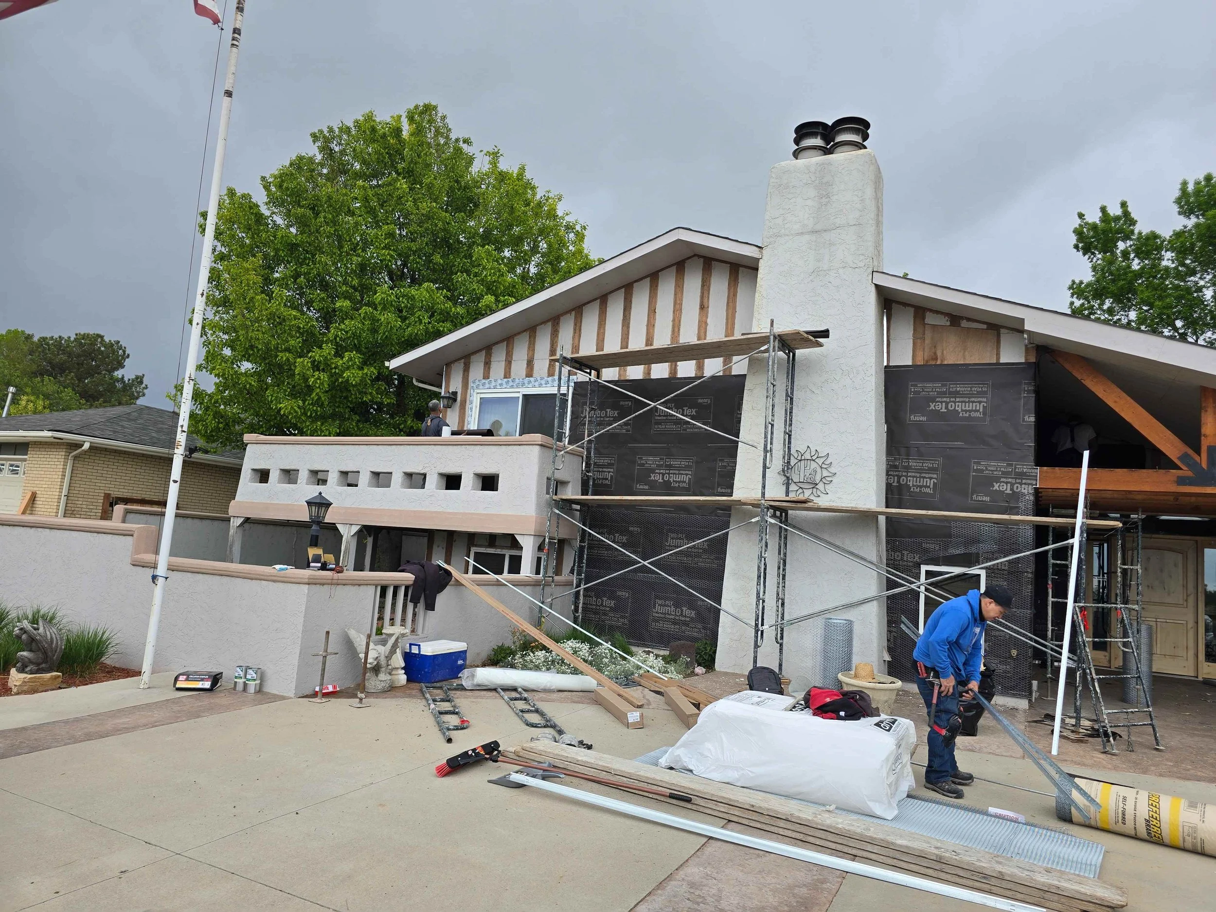Before stucco installation showing exposed wall framing, weather barrier, metal lath and scaffolding on a home exterior.