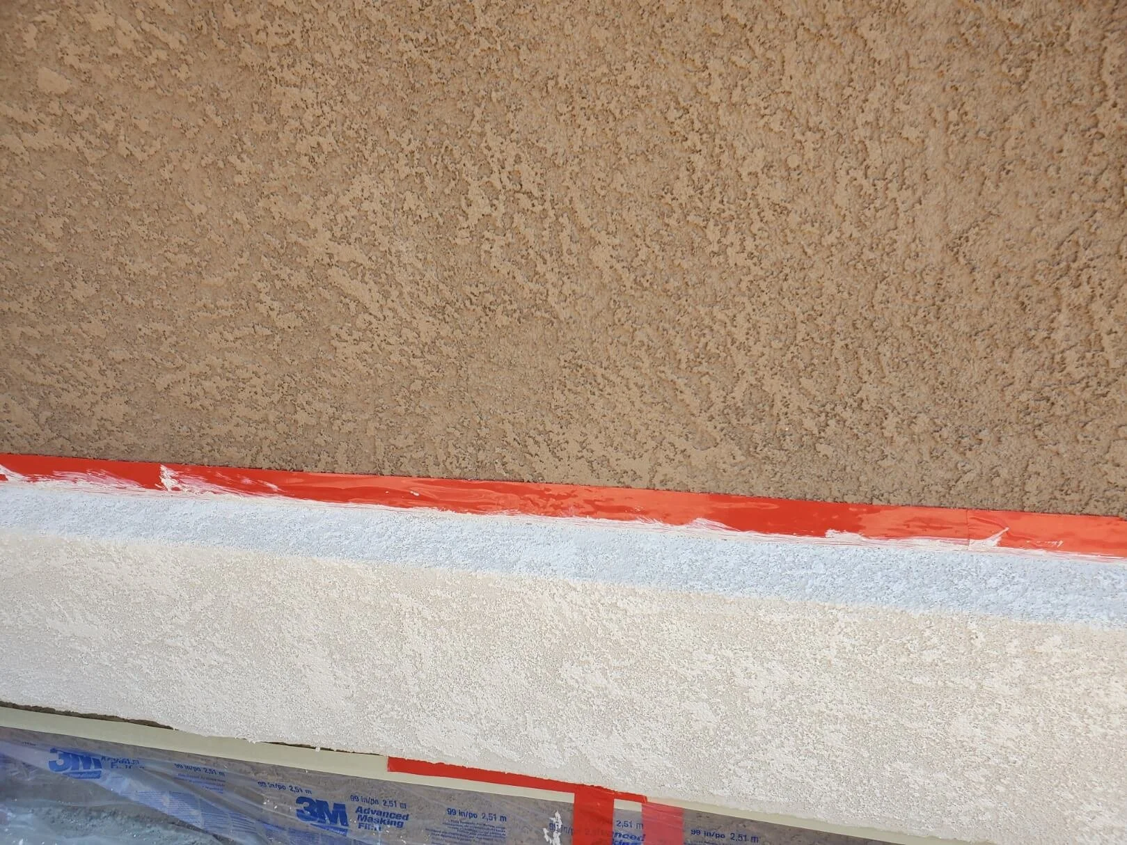 Close-up of a textured beige stucco wall with red tape and a white painted area below. Texture matching, color matching Johnstown Colorado