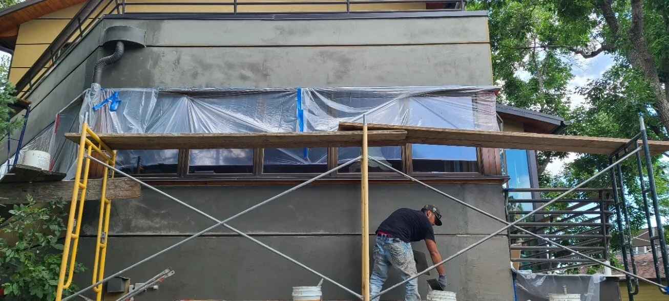 Construction worker applying stucco to a building exterior using scaffolding.