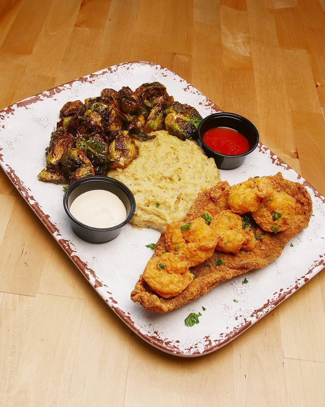 Fried shrimp platter with mashed potatoes, brussels sprouts, and dipping sauces.