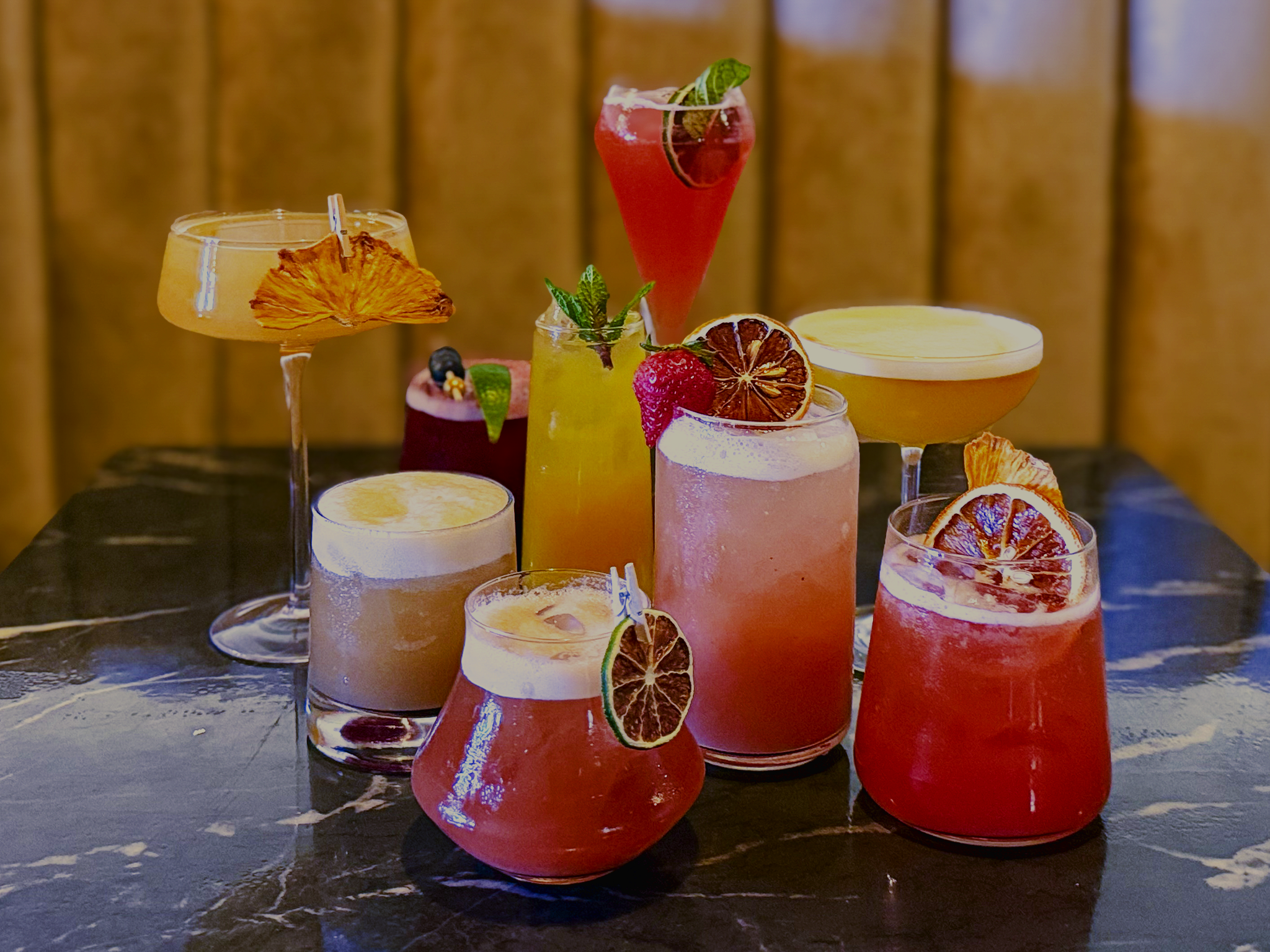 Variety of colorful handcrafted cocktails on a dark marble bar for happy hour.