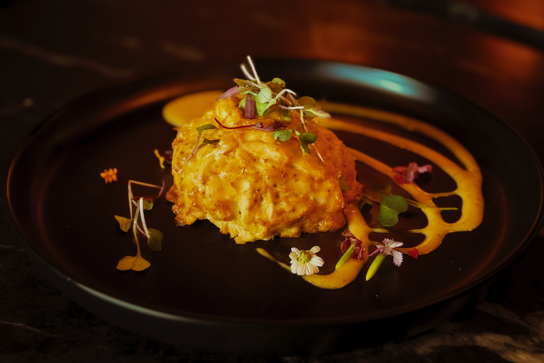 Signature jumbo lump crab cake with elegant sauce swirls and microgreen garnish.