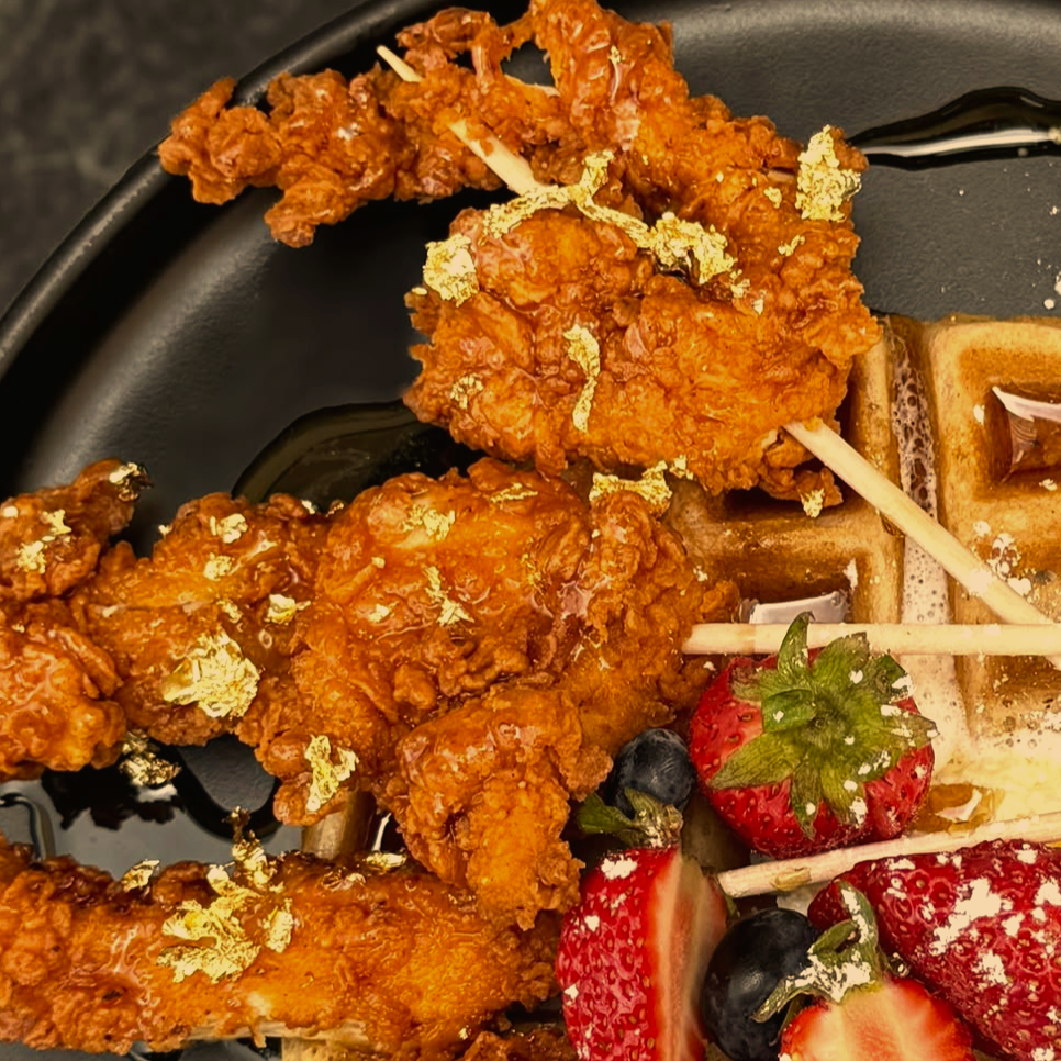 Crispy chicken and waffles appetizer with fresh strawberries and gold leaf garnish.
