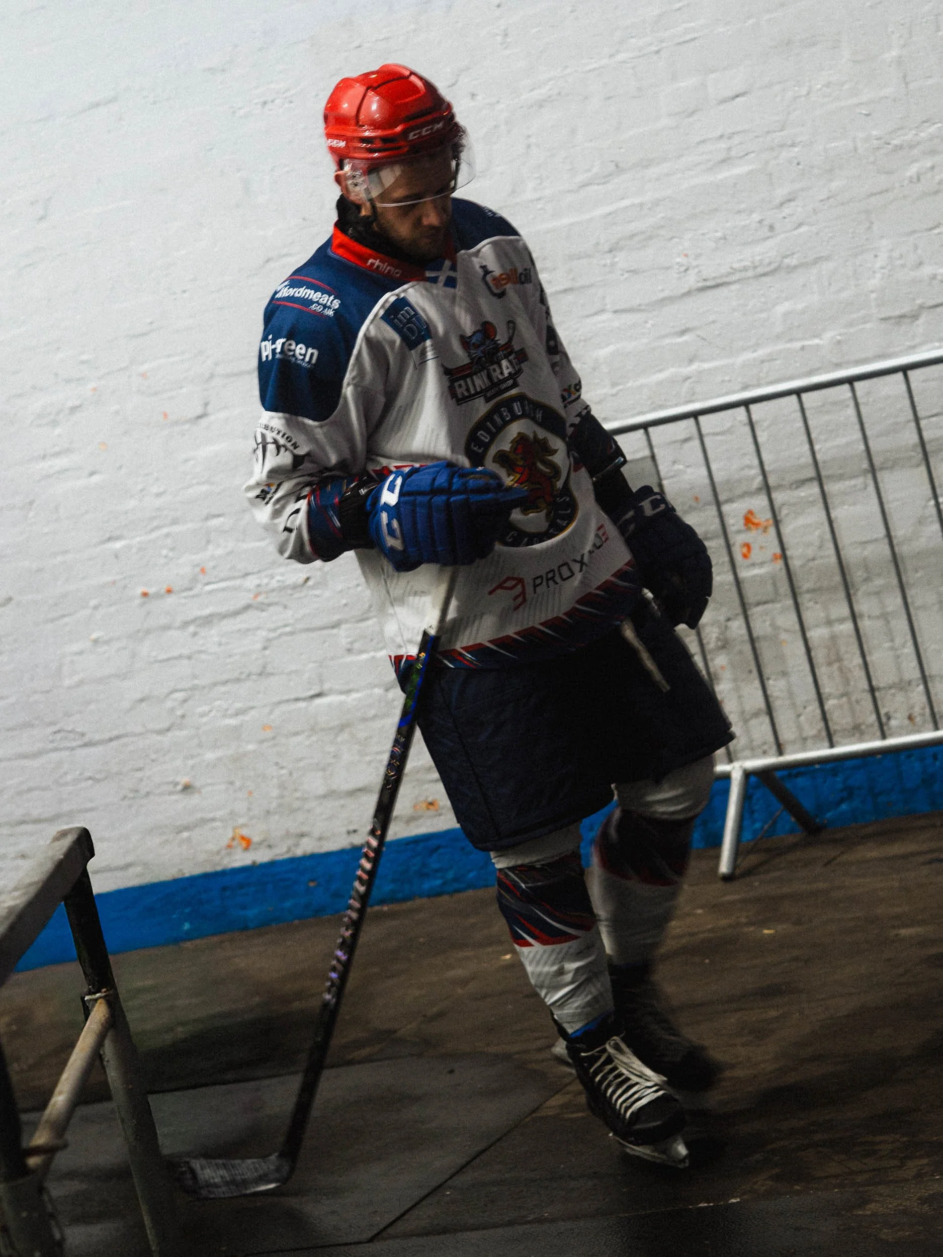 An ice hockey player dressed in a white and blue uniform with a red helmet, in a hockey rink.