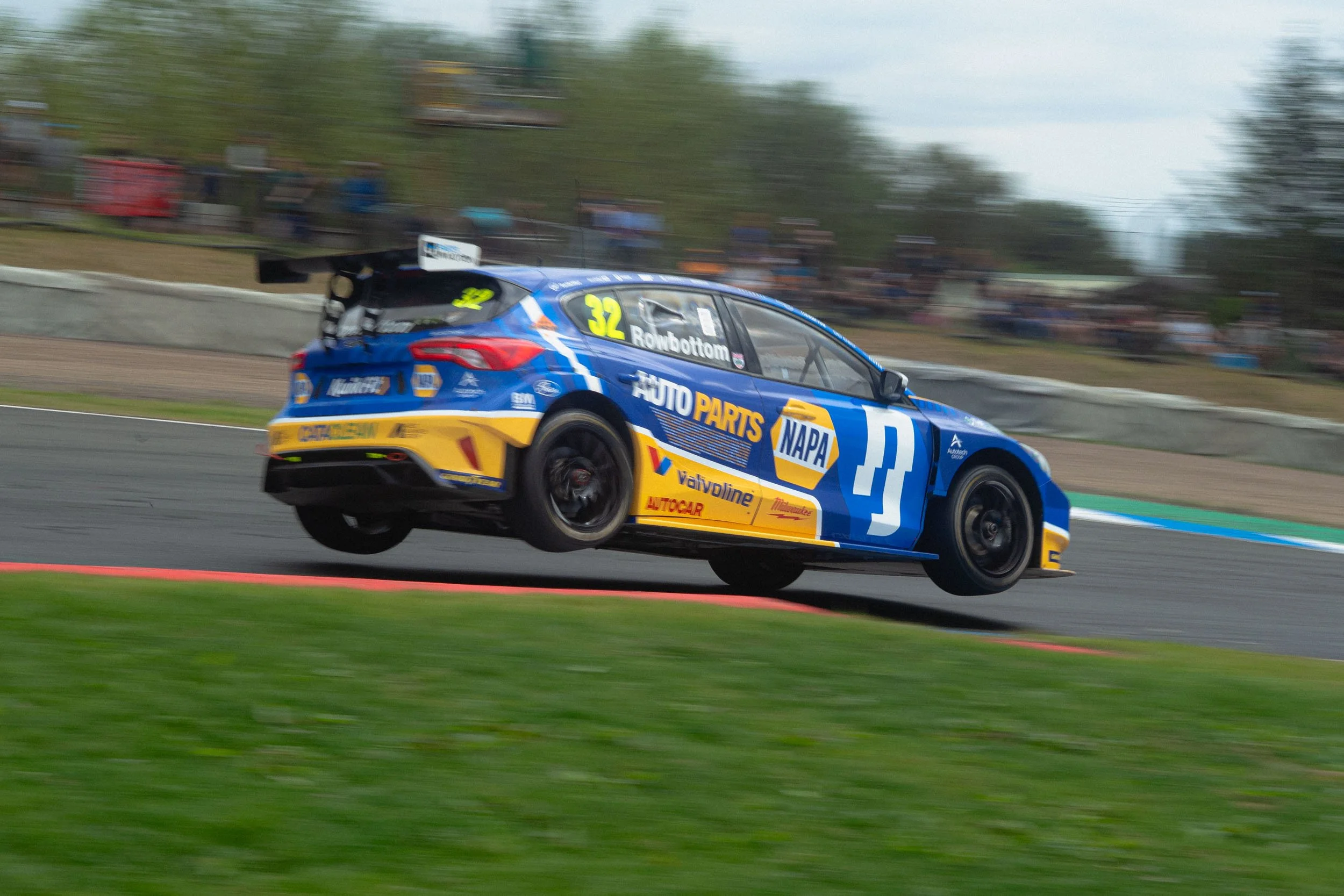 A race car in blue and yellow livery with the number 32, airborne above a race track during a motorsport event.