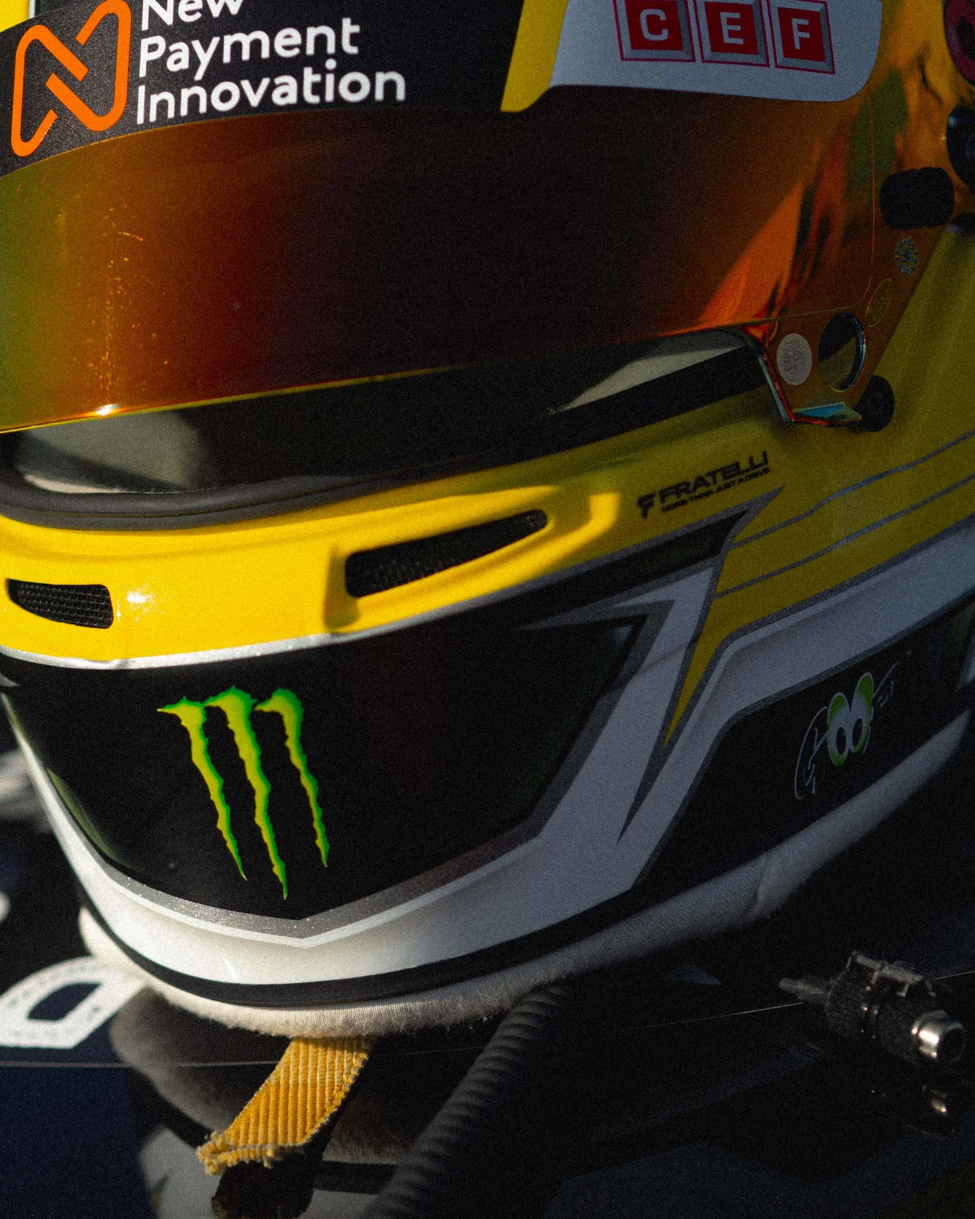 Close-up of a racing helmet with black, yellow, and red colors, featuring Monster Energy and other sponsor logos.