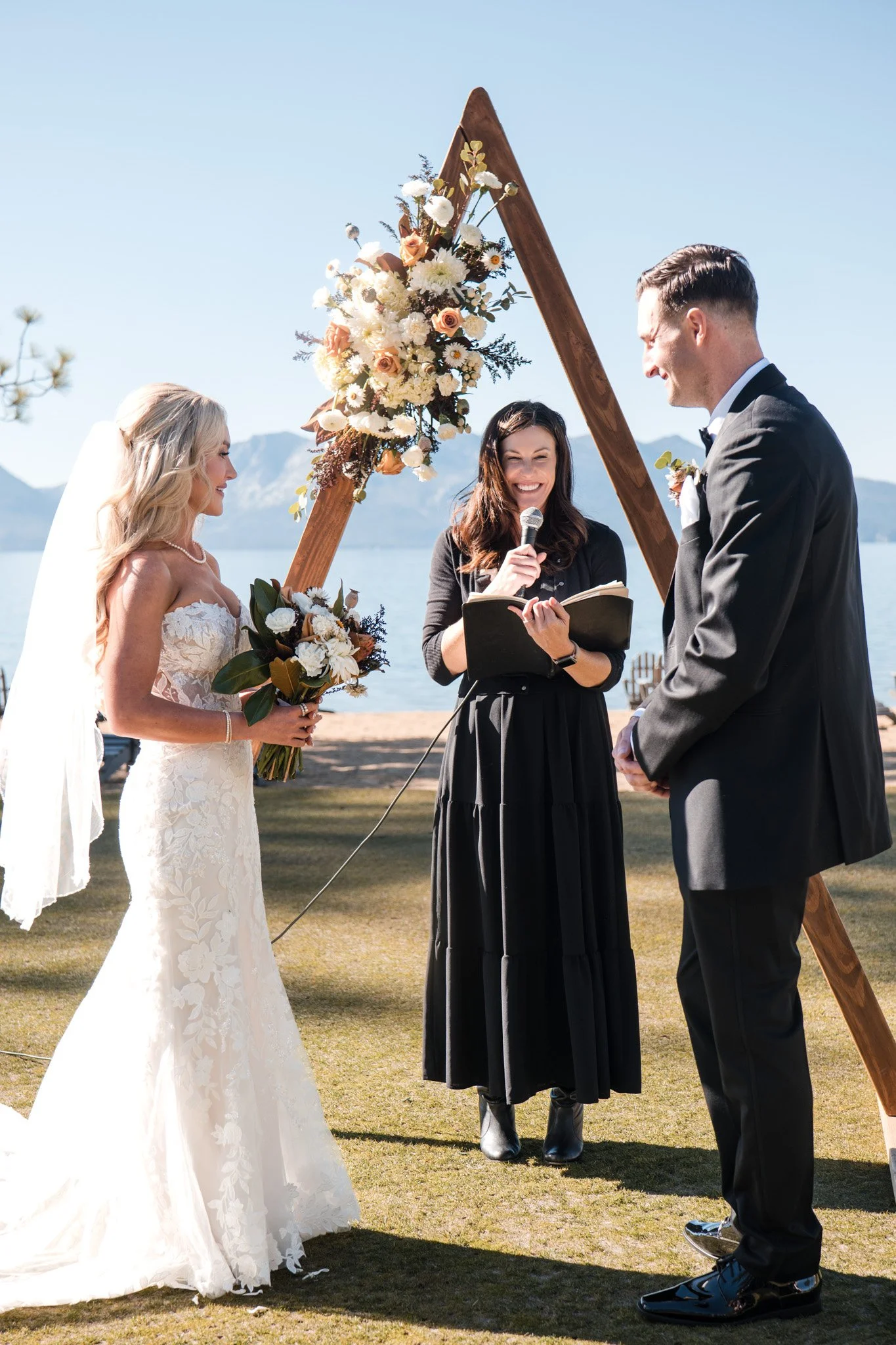 An Edgewood wedding couple getting married outdoors by Lake Tahoe, exchanging vows under a decorated wooden arch with flowers from Pomegranate Occasions, with an officiant from Pomegranate Occasions.