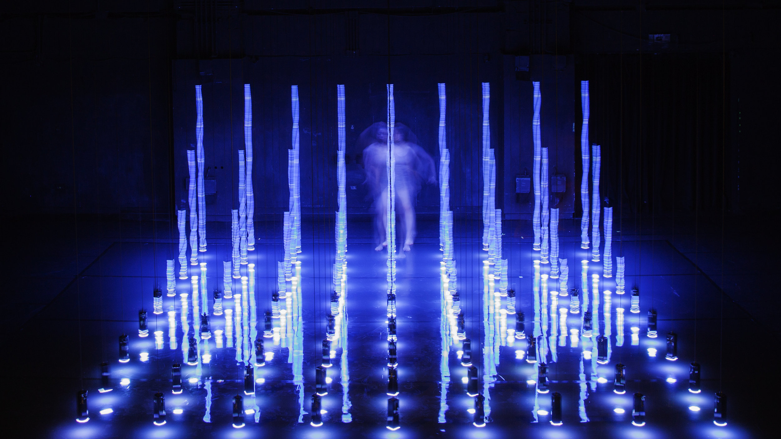 Su Wen-Chi studies the place of the human body in a world dominated by technology. Through this installation-performance, the Taiwanese dancer and choreographer performs a solo show as beautiful as it is disturbing. Alone on stage, Su Wen-Chi dances in a dark space equipped with a moving sound and light grid pattern. More precisely, it is a motorized system made of 81 rectangular hanging objects. Each one is equipped with a LED and a small speaker. The installation seems alive and appears oppressive, even menacing. It perfectly embodies how technology has invaded our cities and our lives. The dancer who has become an androgynous being is struggling against an interactive virtual “wave”. Then, the Yilab company’s founder begins to perform a both demanding and sensual strange ballet, representing the struggle between man and machine, nature and synthetic, reality and the virtual world with some unknown language.