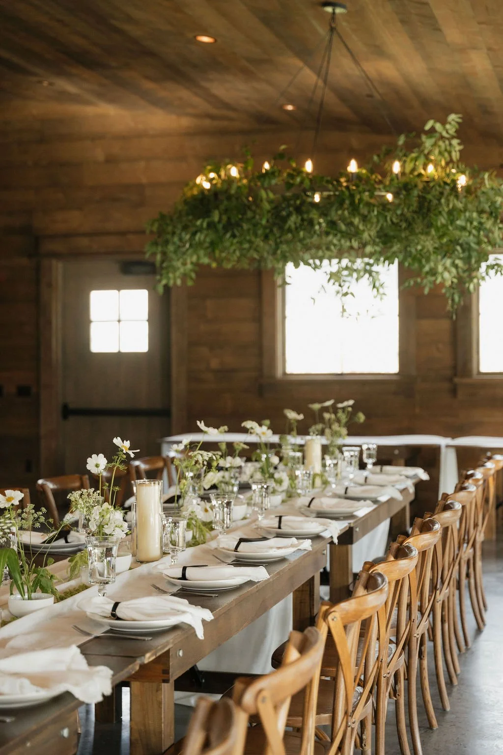 bentwood chair with farmhouse tables with a white runner and white flowers,  candles and ikebana with greenery on the chandeliers at copper rose ranch