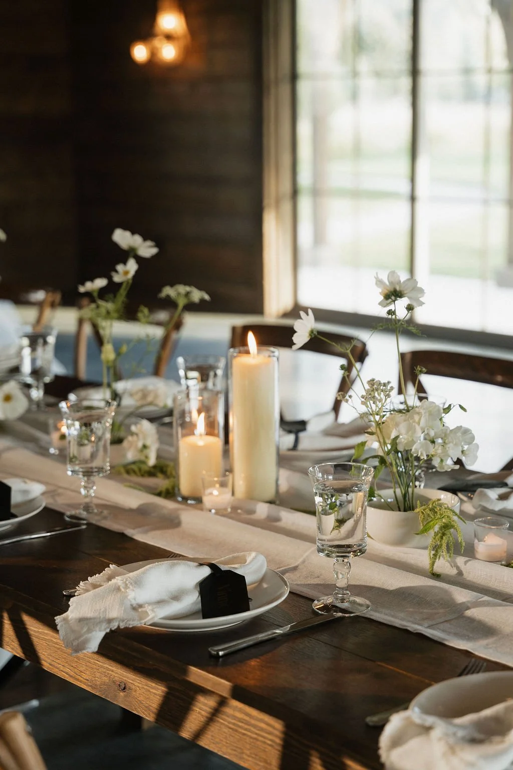 the ikebana table settings with the candles lit on farmhouse tables with black bag tags for place cards