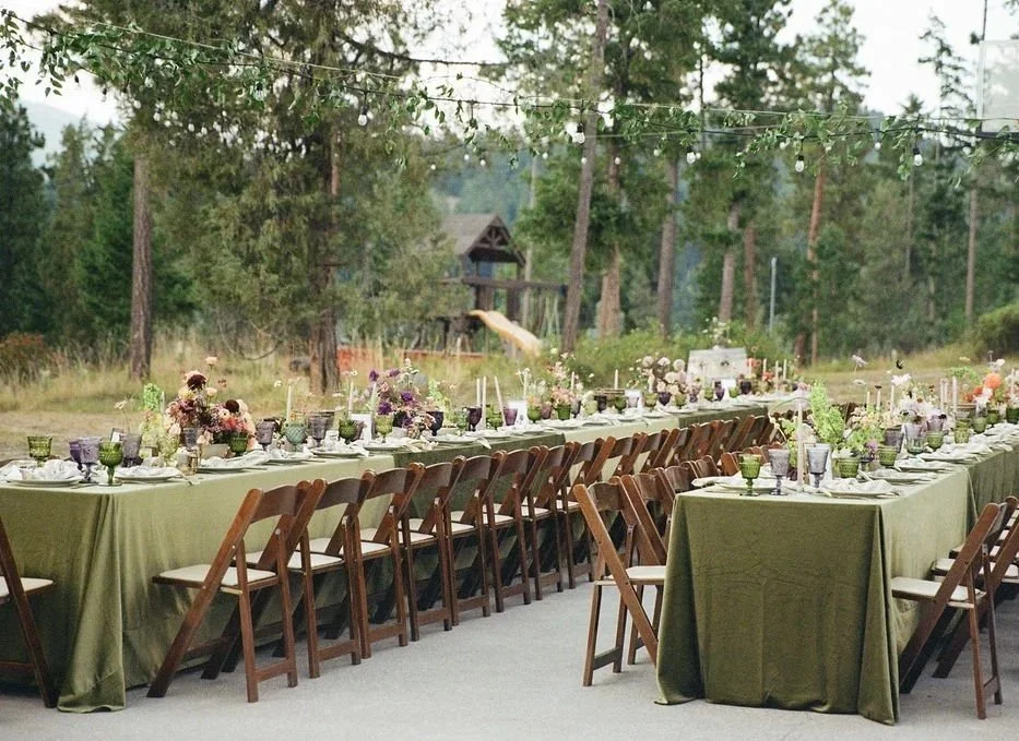 a wide angle shot of the reception tables with green linens, goblets, centerpieces and ikebana with purple, burgundy, chartreuse flowers