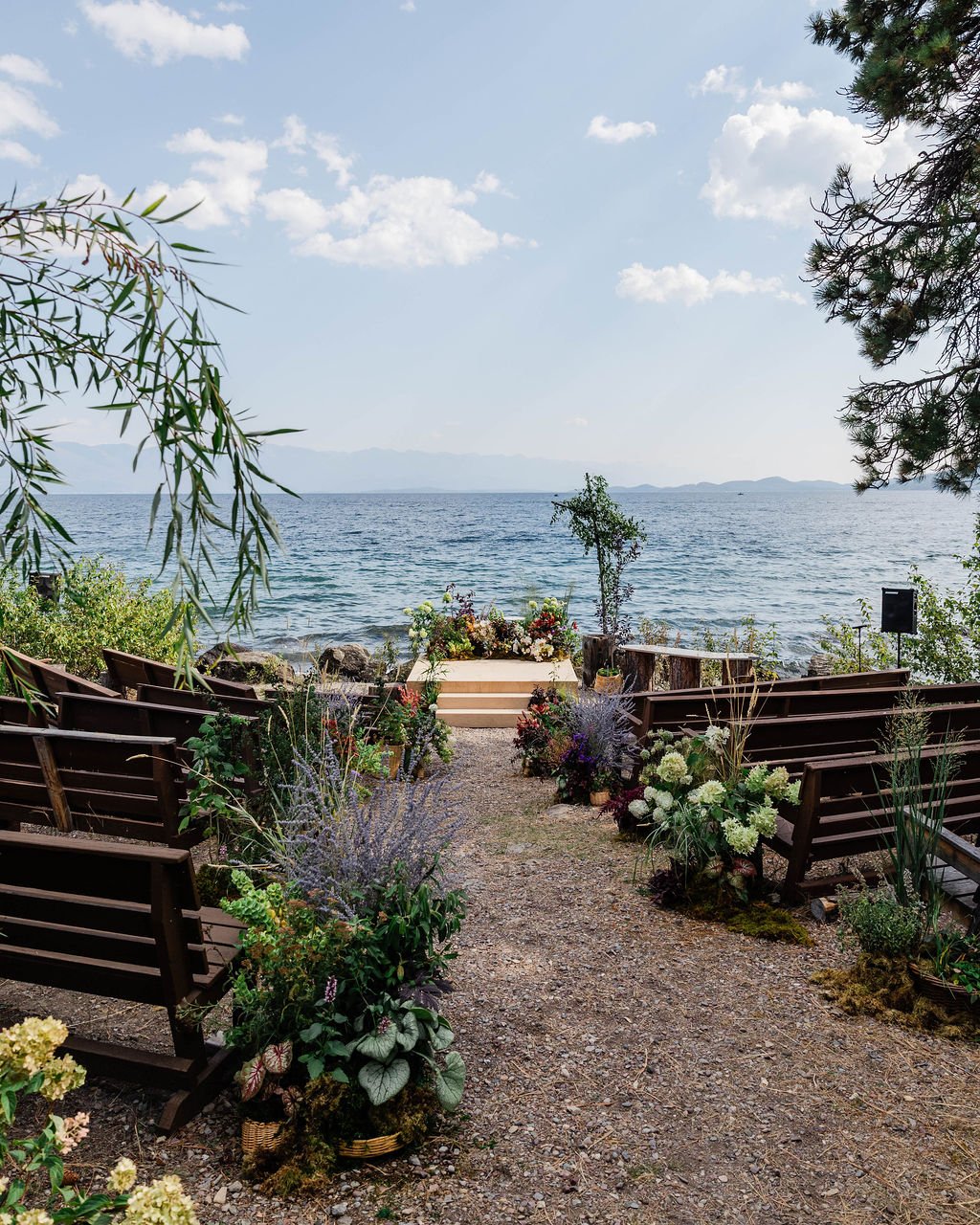 Flathead lake in the background of a wedding ceremony framed by trees and plants in baskets lining the aisle of a wedding with a lush meadow at the front