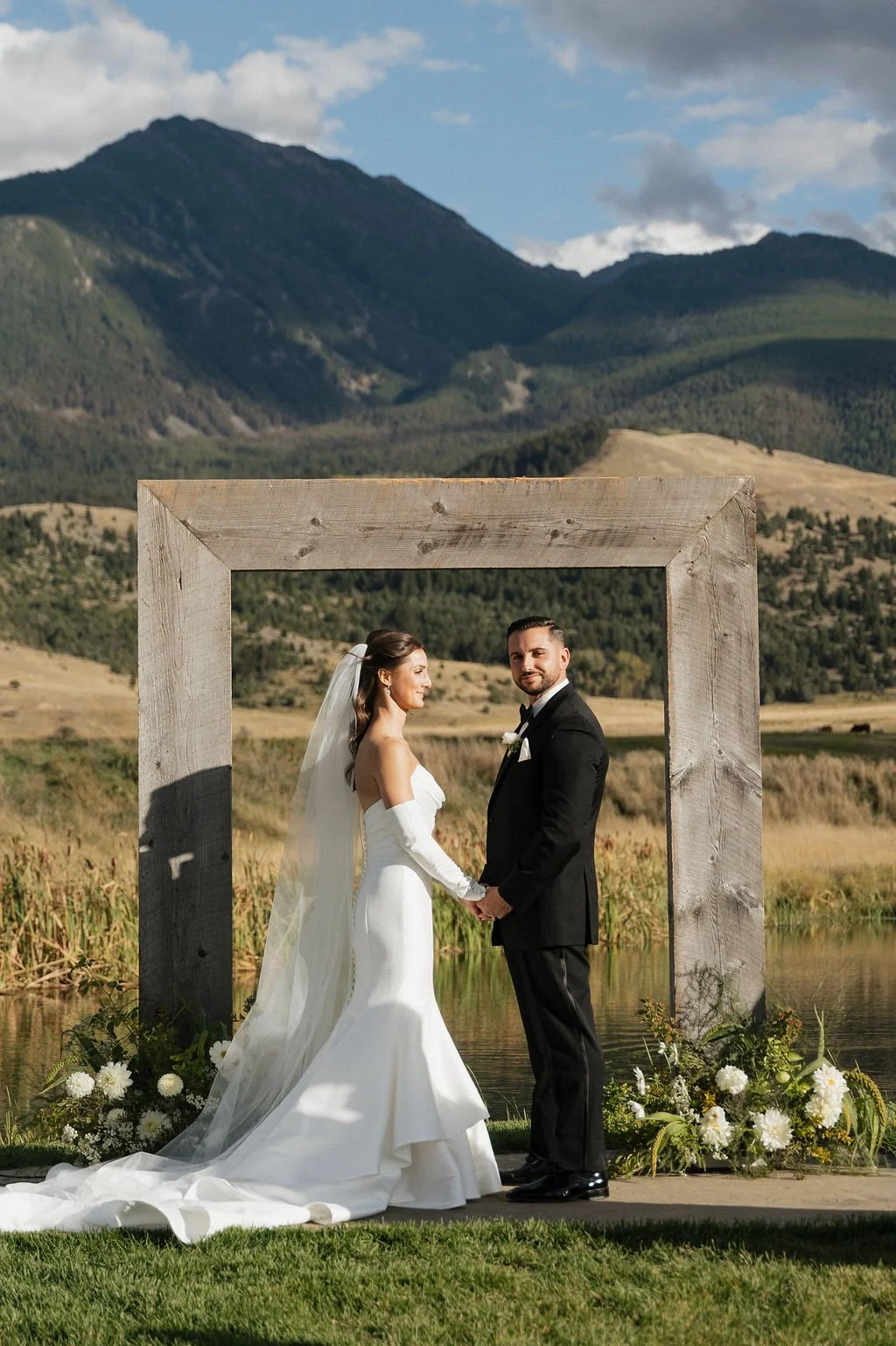 another but with really cute expressions on the bride and groom looking out at their guests and smiling with the mountains and arch behind