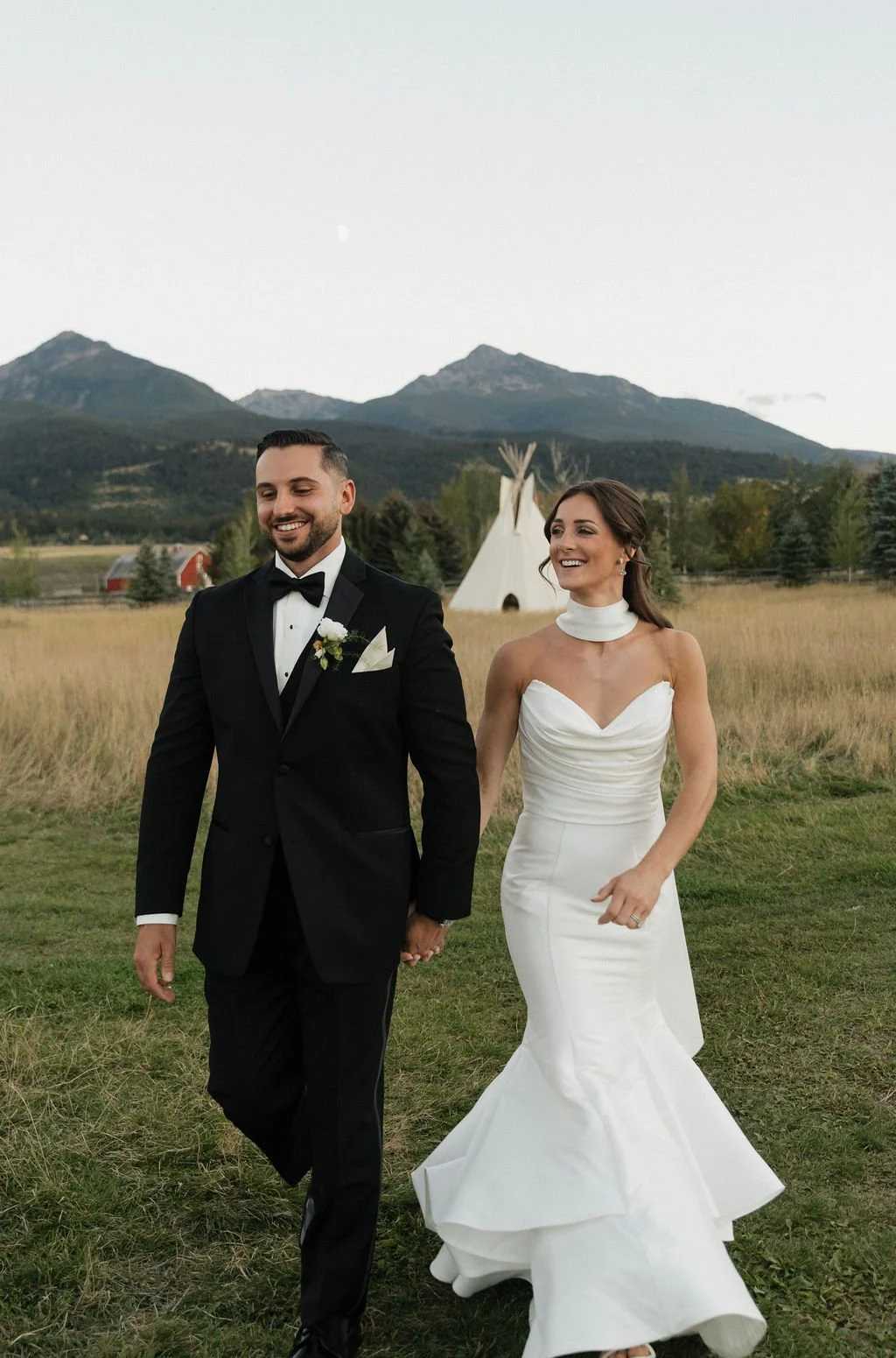 golden hour photos with the sun on the mountains and the bride and groom holding hands and looking in different directions with the mountains and tipi in the background