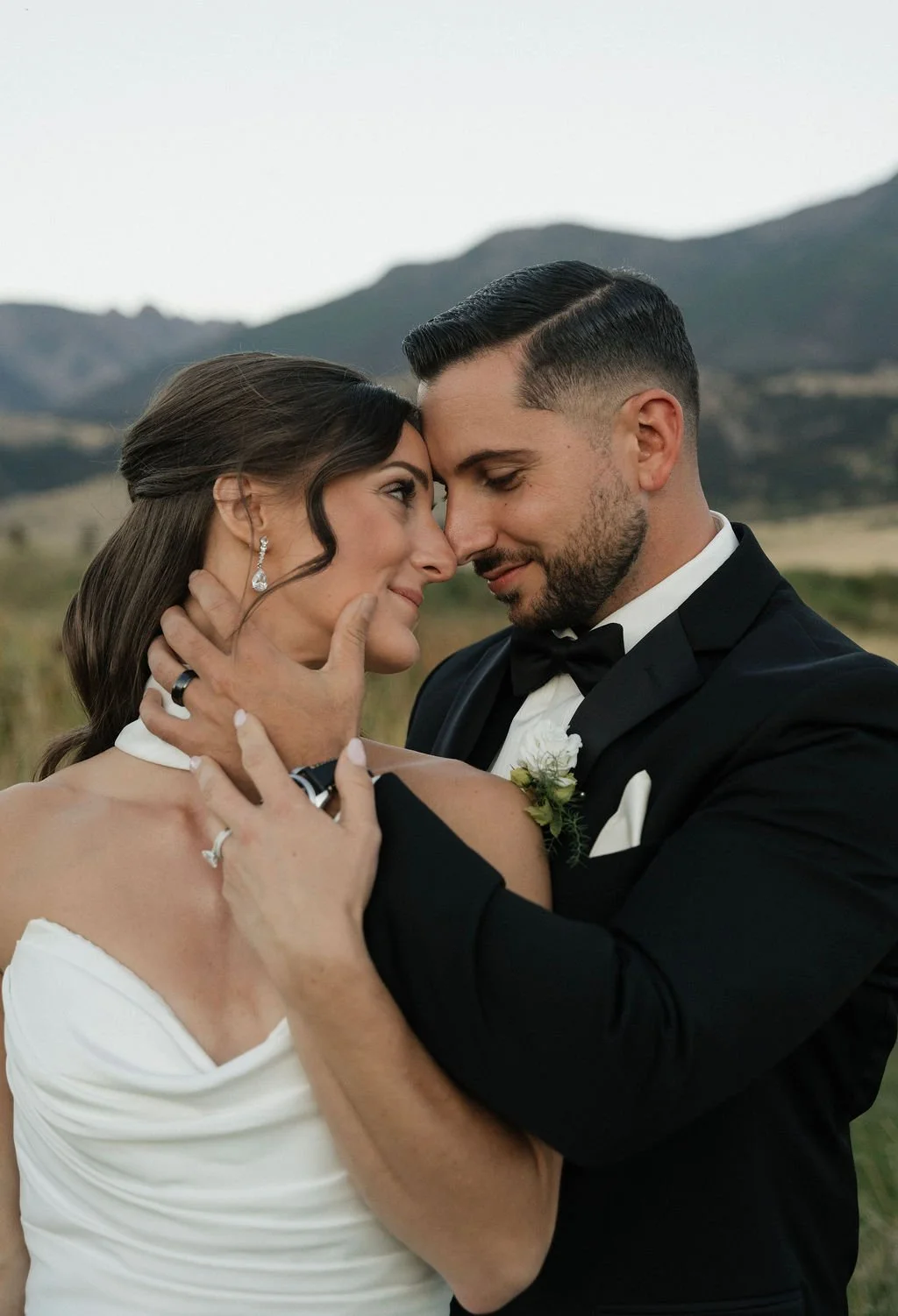 golden hour photos with the groom holding the bride's face and her hand on his with their rings with the sun on the mountains 