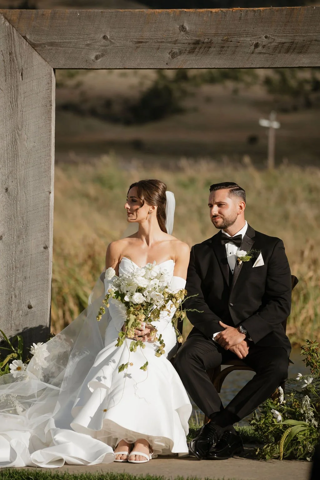 a vertical closer photo of the bride and groom sitting listening to the catholic ceremony with the bride holding her bouquet her posture is amazing