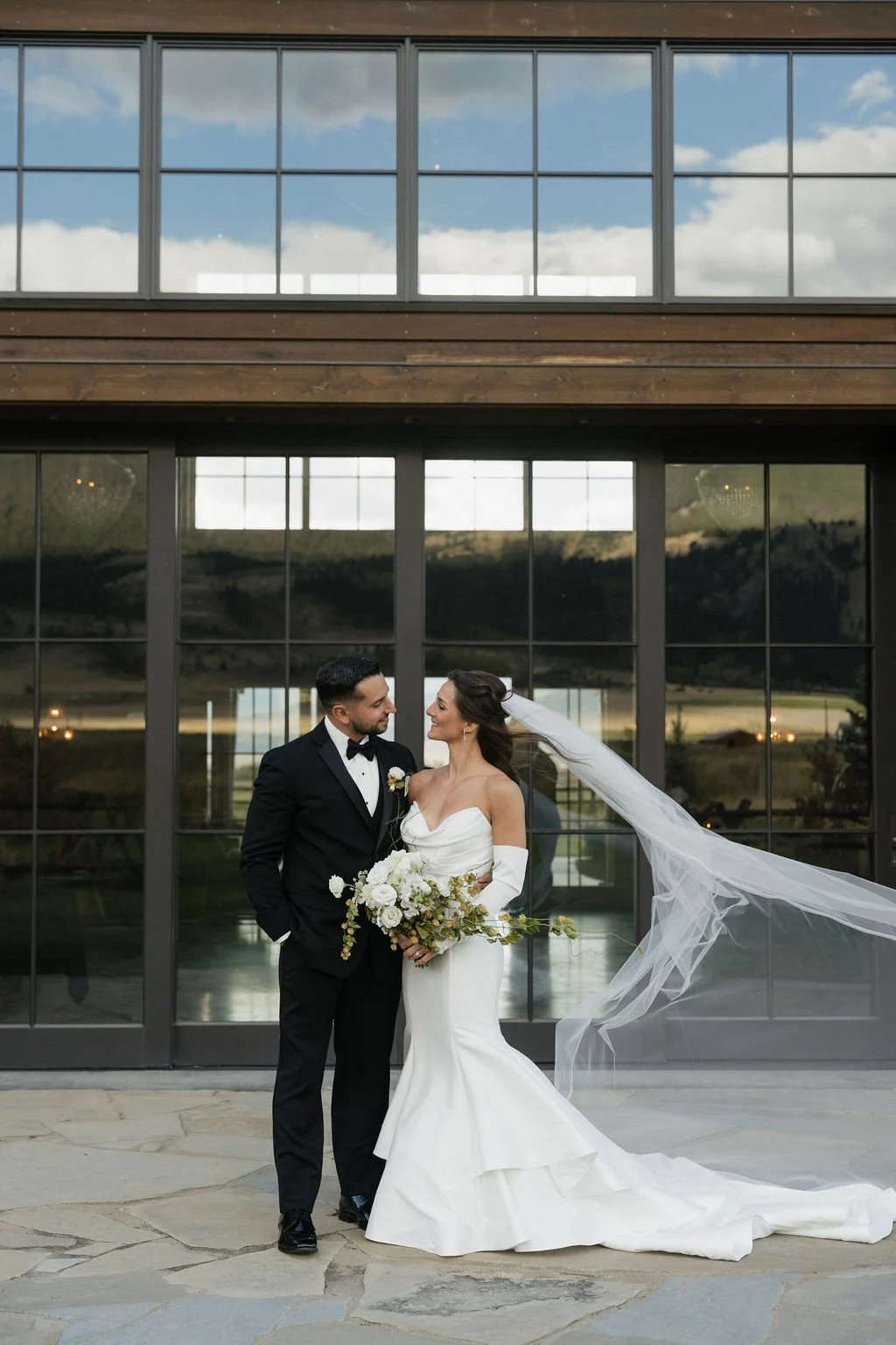 portrait of the bride and groom looking at each other outside of the barn at copper rose ranch with the bride's veil blowing in the wind