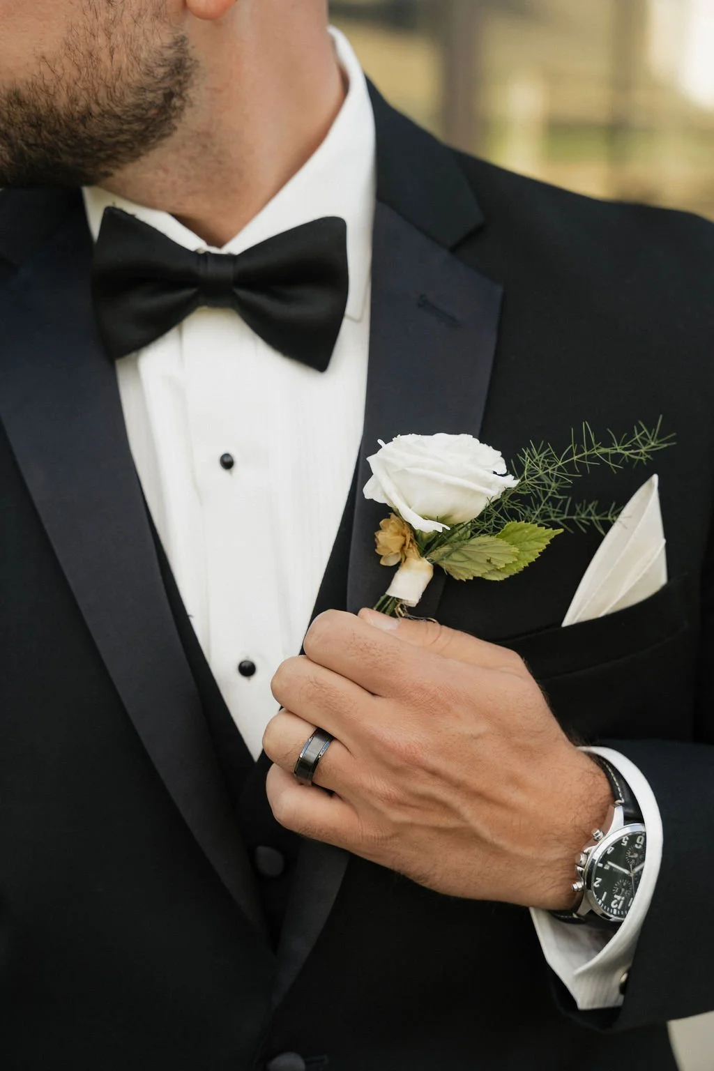 close up shot of the groom with his hand on his lapelle with his ring watch bow tie tux pocket square and boutonniere