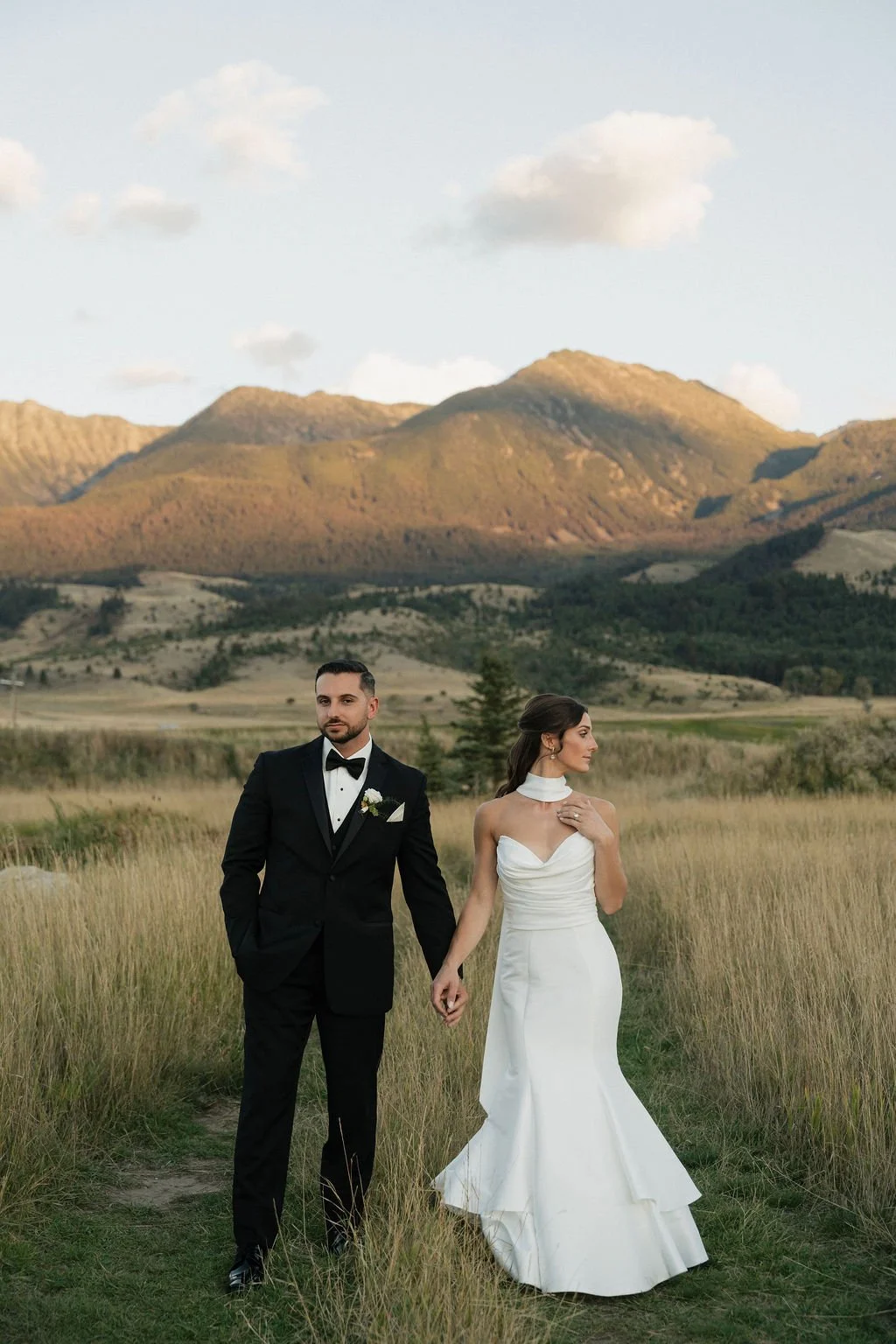 goldenhour photos with the sun on the mountains and the bride and groom holding hands and looking in different directions
