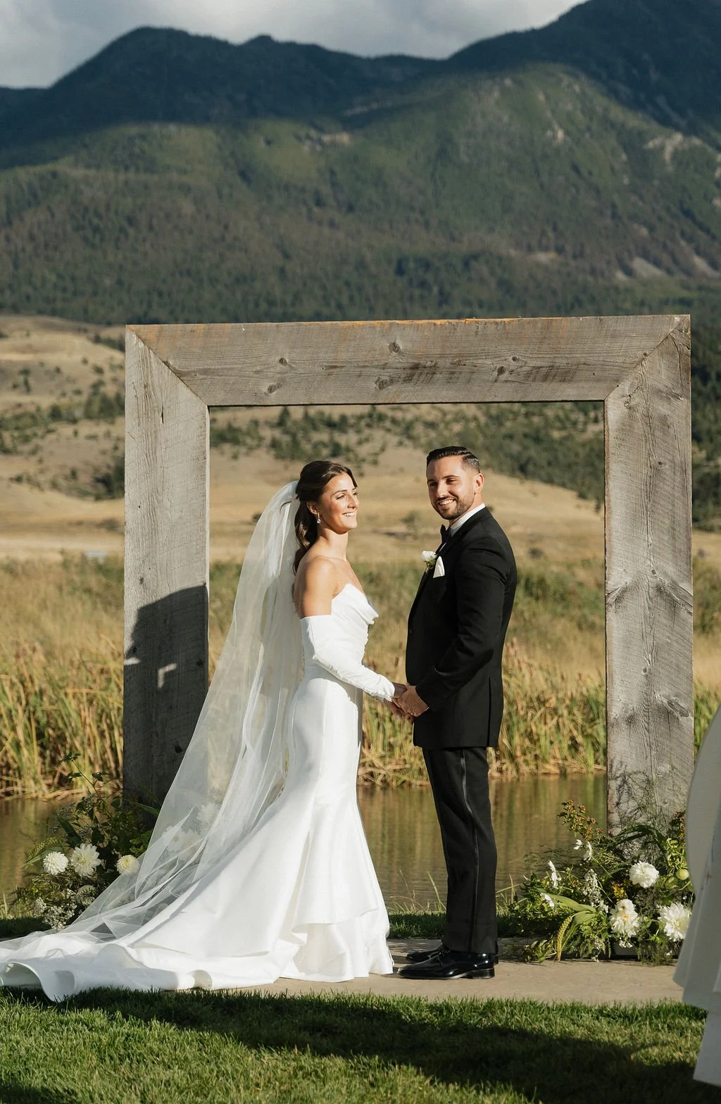 the bride and groom looking out at their guests and smiling with the mountains and arch behind