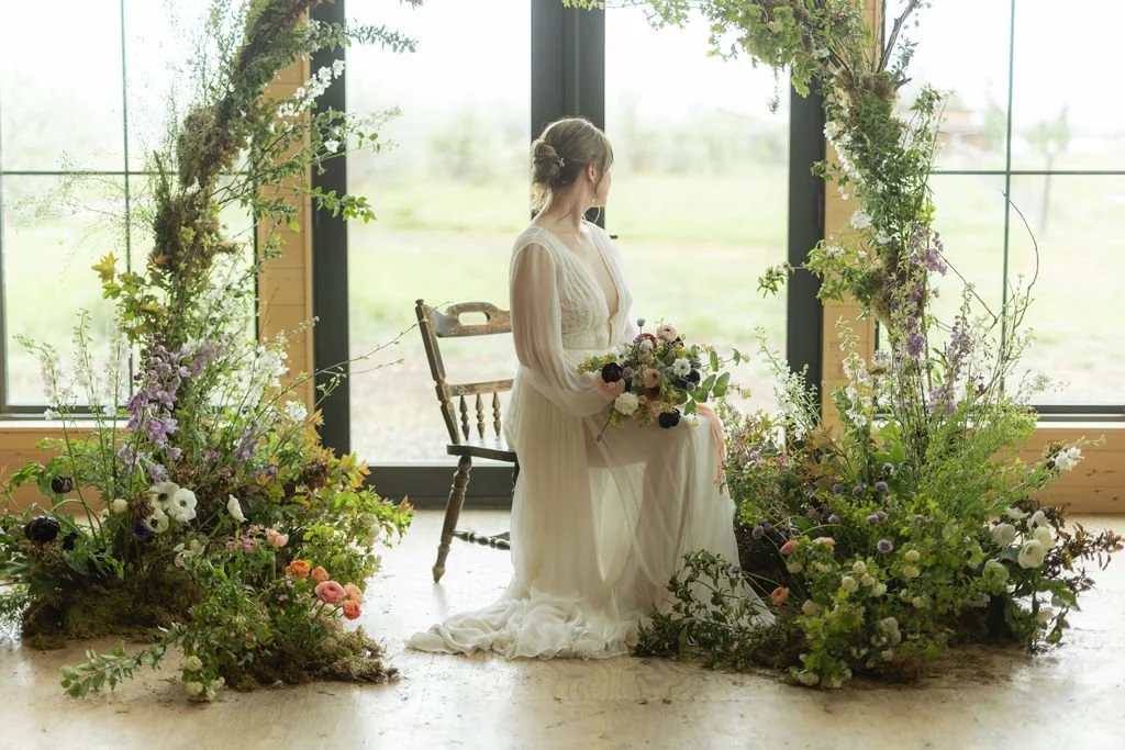 Bozeman montana florist Wedding floral arch with bride sitting in it with floral meadow